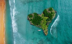 An aerial view of a heart-shaped island beach with clear blue water.